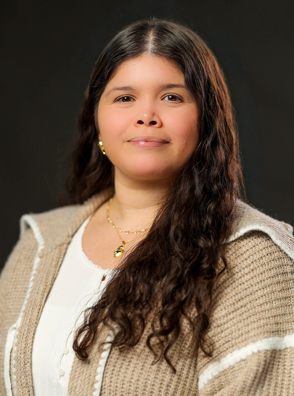 Portrait of a woman with long dark hair wearing a beige sweater against a dark background