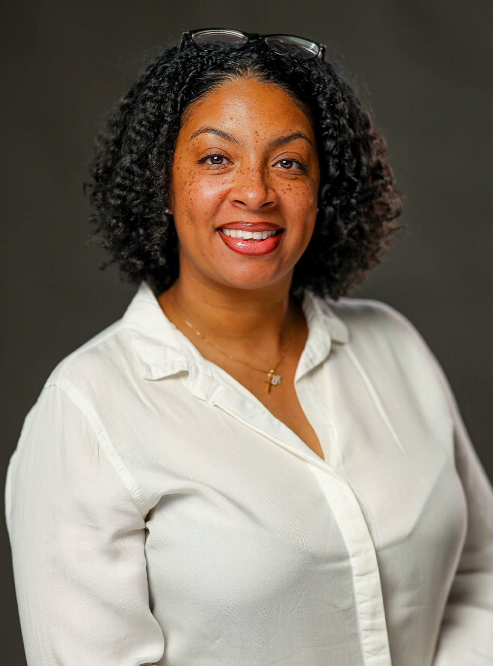 Portrait of a smiling woman with long brown curly hair wearing a white top against a dark background