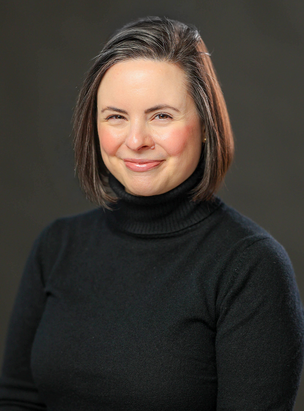 Portrait of a smiling woman with short brown hair wearing a black top against a dark background