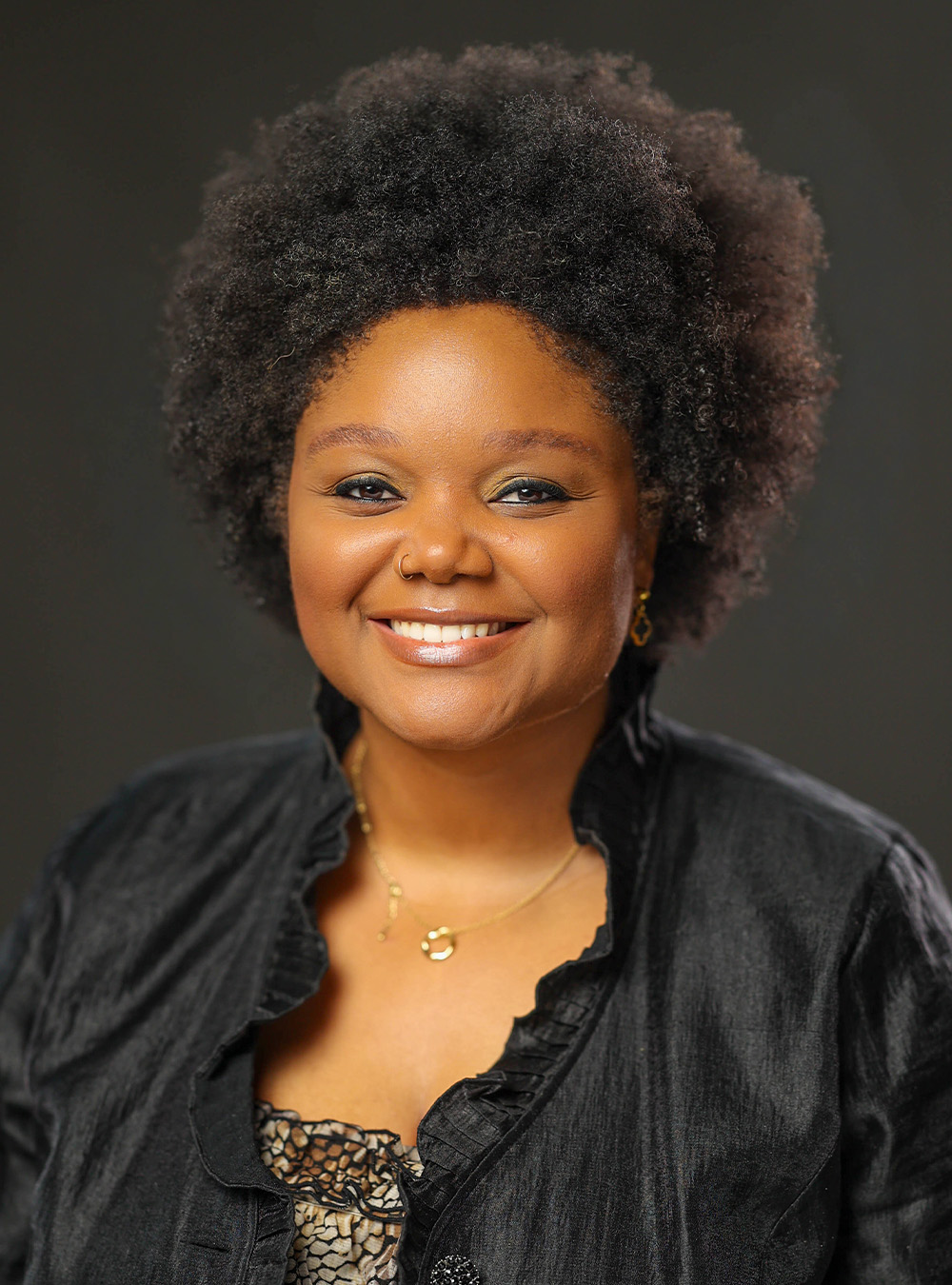 Portrait of a smiling woman with natural curly hair wearing a black top against a dark background