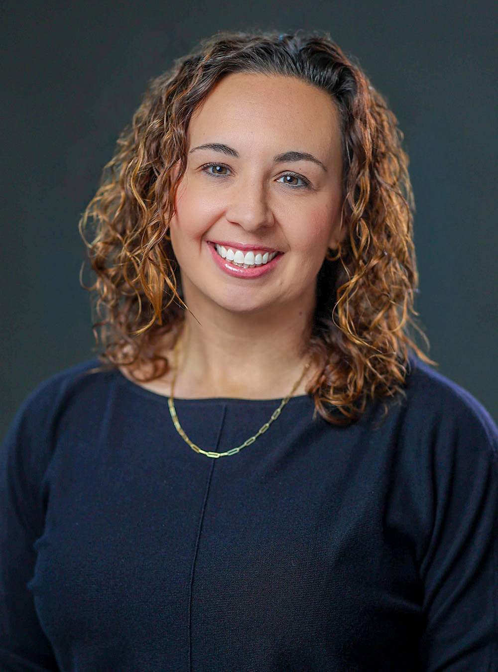 Portrait of a smiling woman with sholder=length brown hair wearing a blue top against a dark background