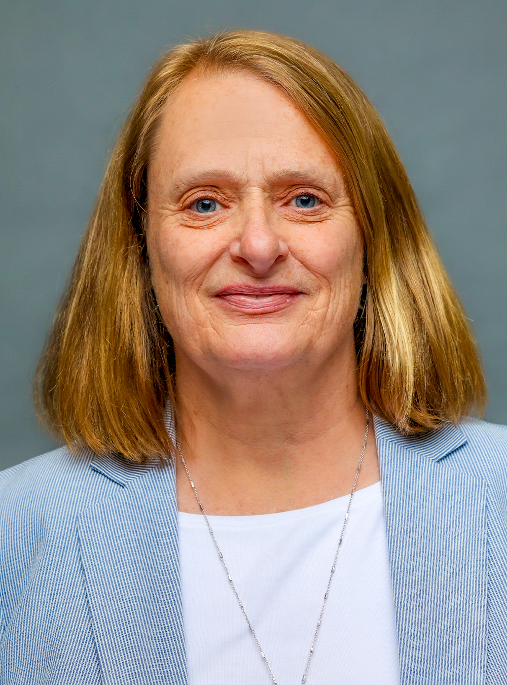 Portrait of a smiling woman with sholder-length blonde hair wearing a white shirt and navy and white striped jacket against a neutral background