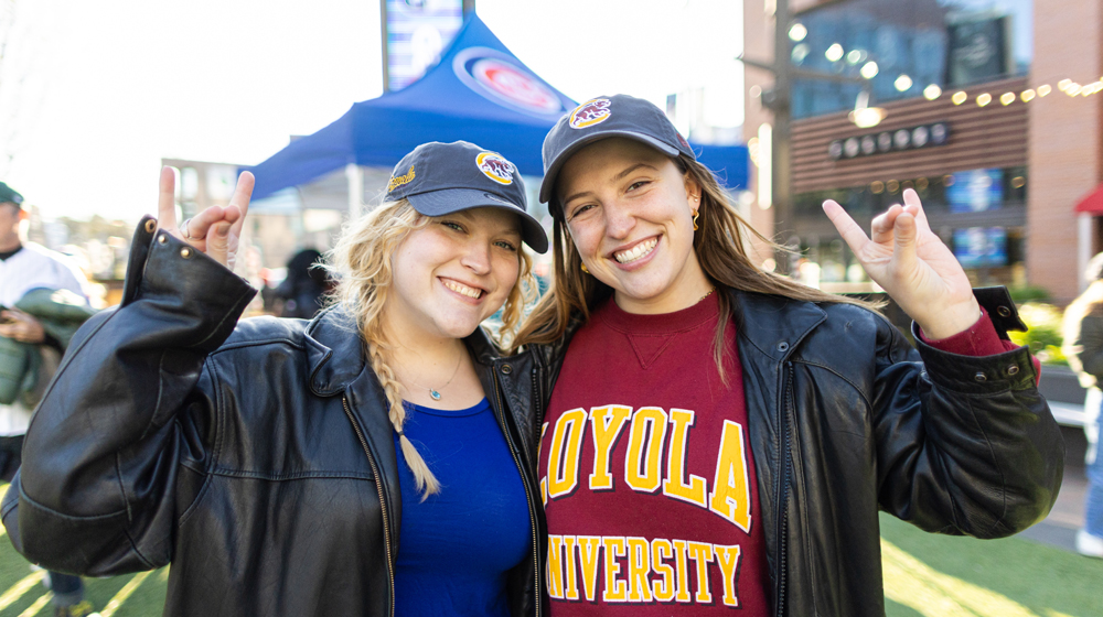 Smiling alumnae in Loyola tee shirt and caps at a Cubs Loyola Night.