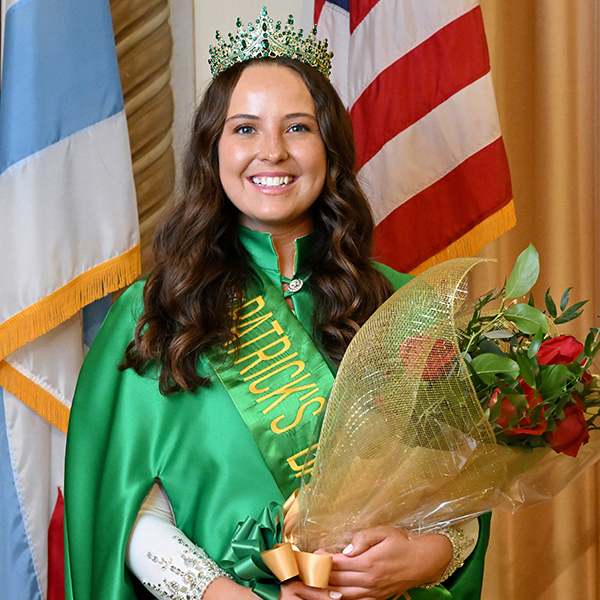 Alumna Cara Walsh in a tiara and sash, holding a bouquet of flowers