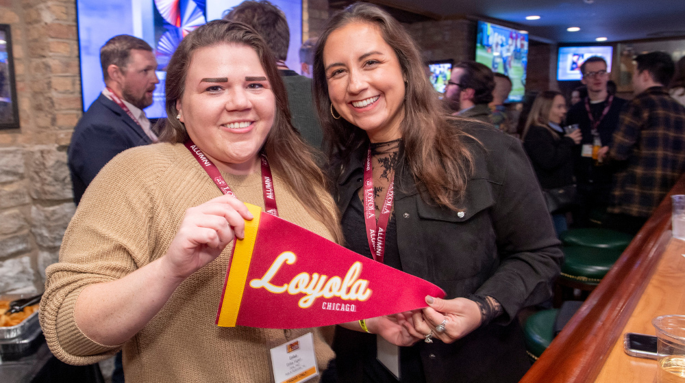 Two alumnae hold a Loyola Chicago pennant.