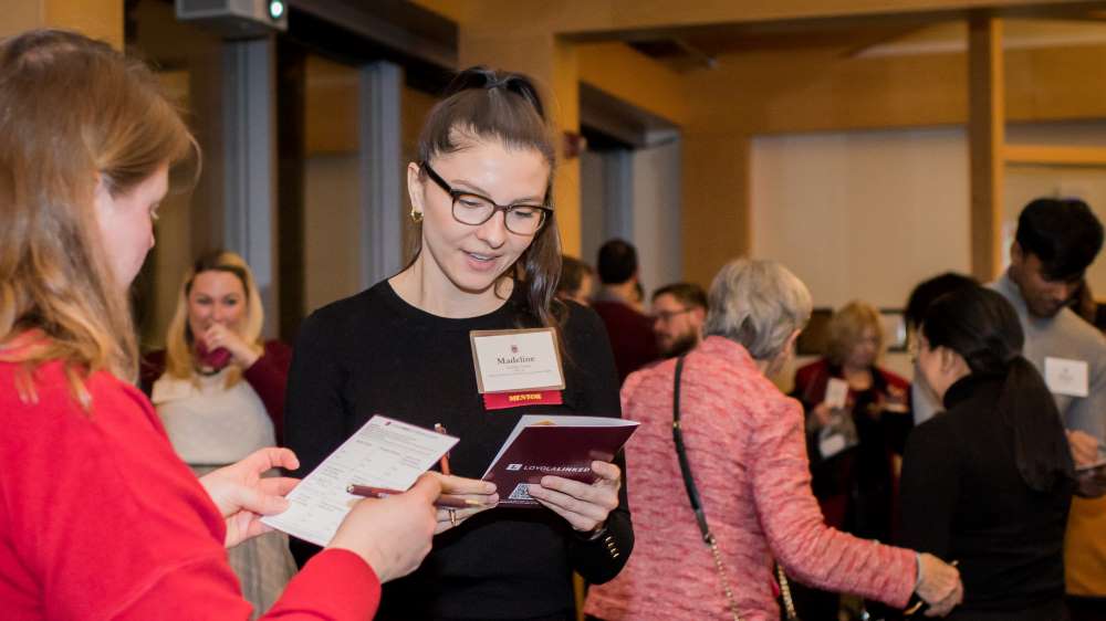 Two alumnae browse brochures about LoyolaLinked and complete forms to become mentors.
