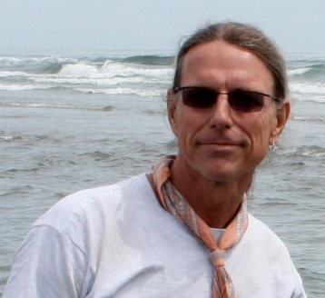 Man wearing sunglasses stands by the ocean with waves in the background