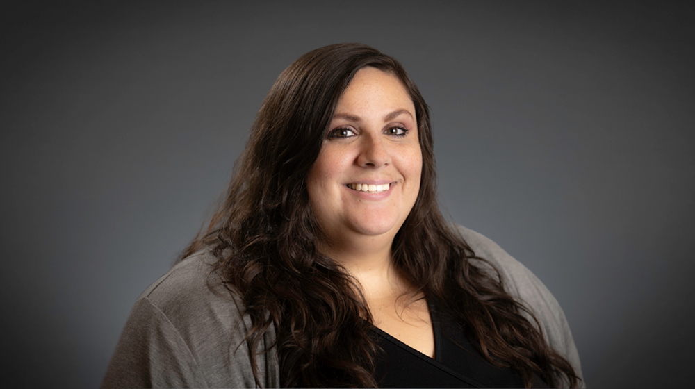 Smiling woman with long wavy hair against a gray background.