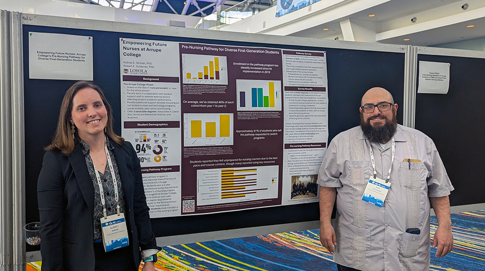 Two people standing beside a presentation poster with charts and text, smiling at the camera