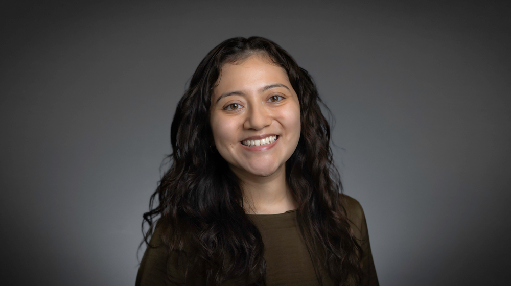 Portrait of a smiling woman with long dark wavy hair against a gray background.