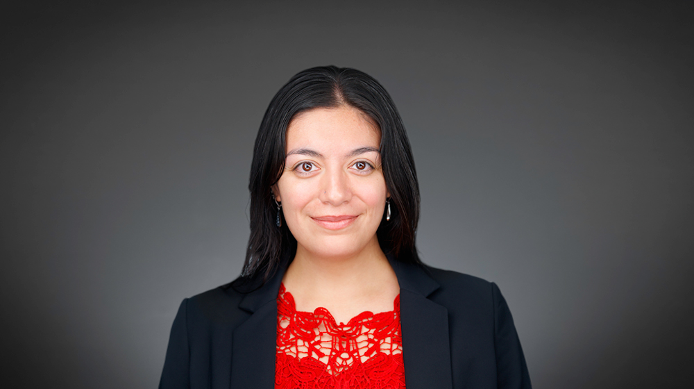 Woman in a black blazer and red top against a gray background