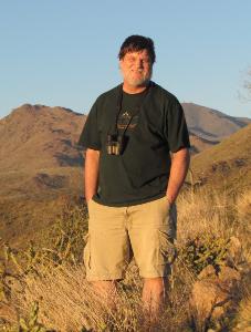 professor wearing a black shirt and tan shorts standing in a grassy field