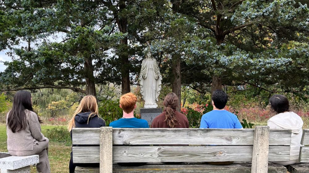 the back of six students heads facing a Mary statue outdoors