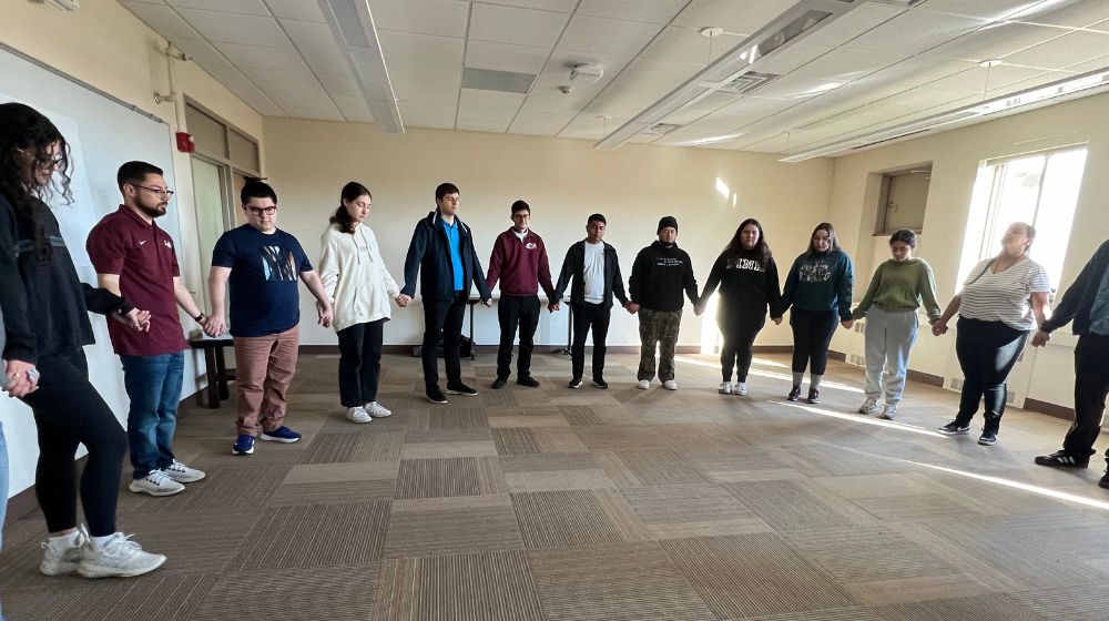 a large group of students stand in a circle holding hands