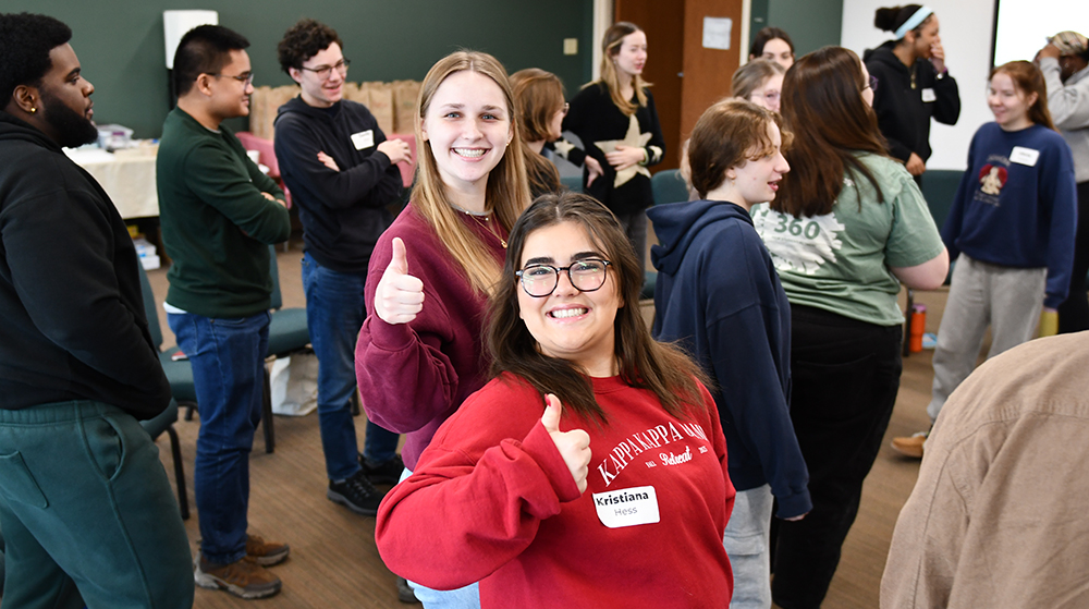 Two students smiling with thumbs up