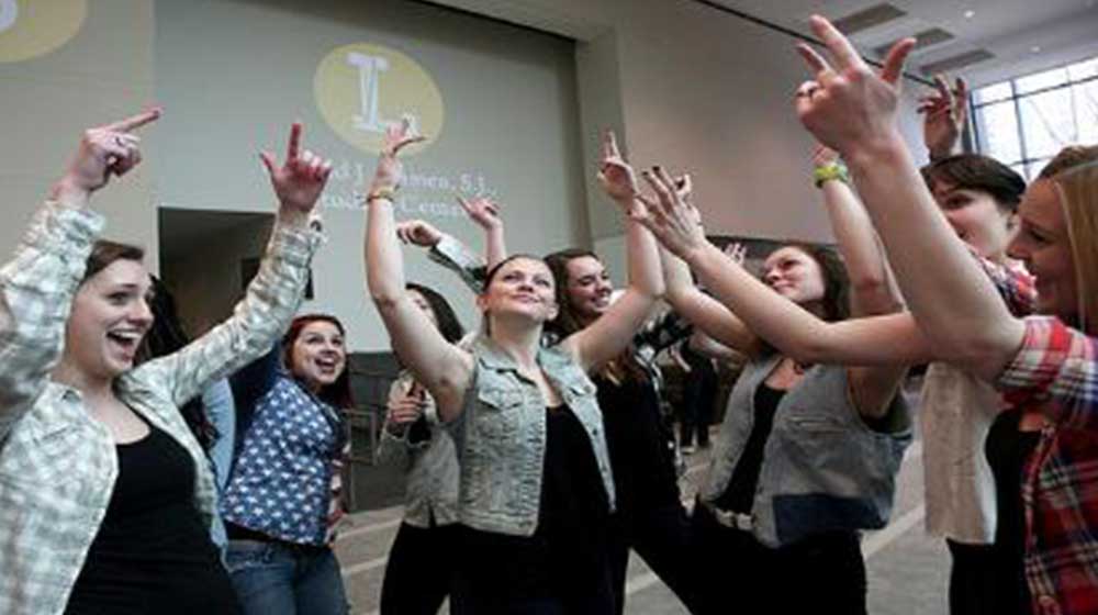 A group of students with their hands in the air performing a group programming excercise
