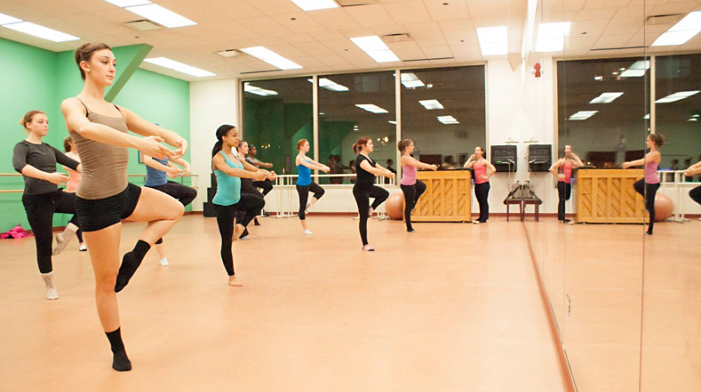 A small group of dance students practice in the studio as an instructor leads.