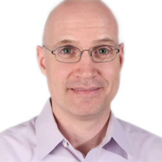 Bald man with glasses wearing a light purple, collared shirt, smiling slightly against a solid white background.