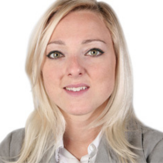 Woman with mid-length blonde hair, wearing a light gray blazer and white shirt, smiling slightly against a solid white background.