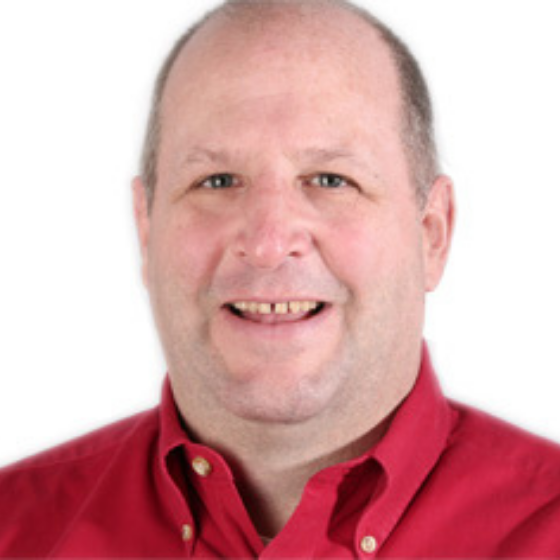 A smiling man wearing a red collared top, against a solid white background.