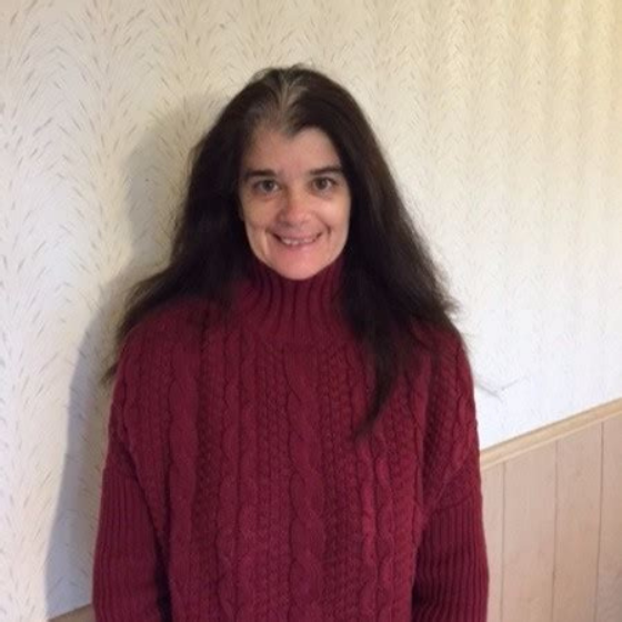 Smiling woman with brown hair, wearing a dark red sweater, standing in front of an off-white background.
