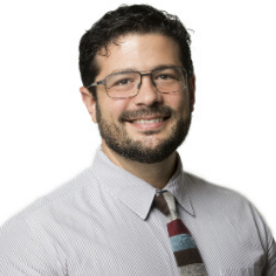 Smiling man with short brown hair, wearing glasses and a striped tie, against a solid white background.
