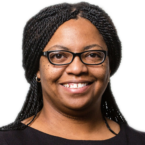 Smiling woman with her long dark brown hair in braids, wearing glasses and a black top, against a solid white background.