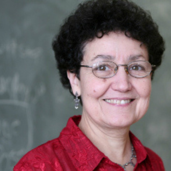 Smiling woman with short, curly dark brown hair, wearing glasses and a collared red top, with a chalkboard in the background.