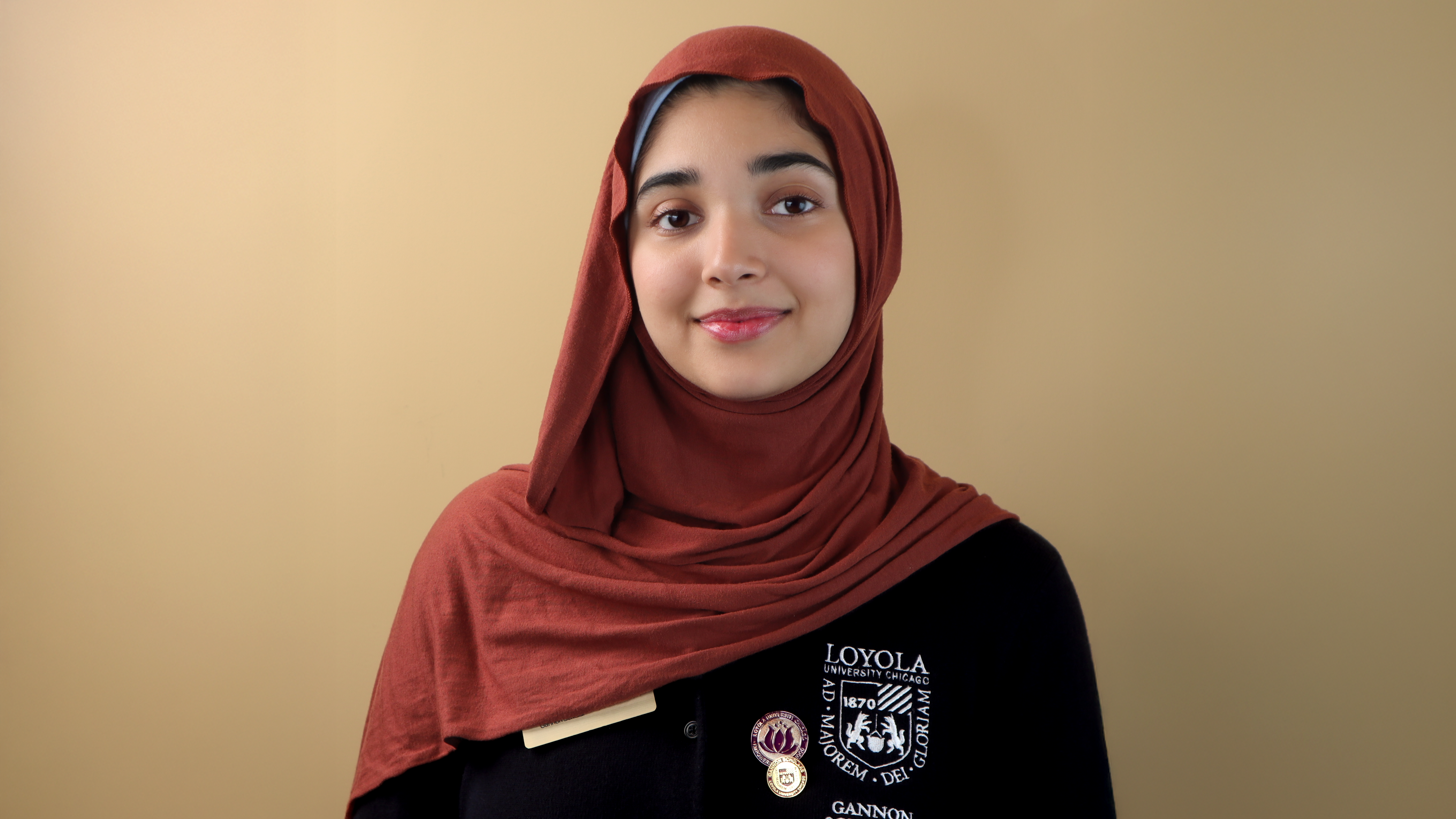 Portrait of Loyola University Chicago student wearing maroon hijab and Loyola Gannon Center shirt against neutral background