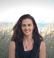 Woman with long dark hair smiling outdoors with tall grasses in the background
