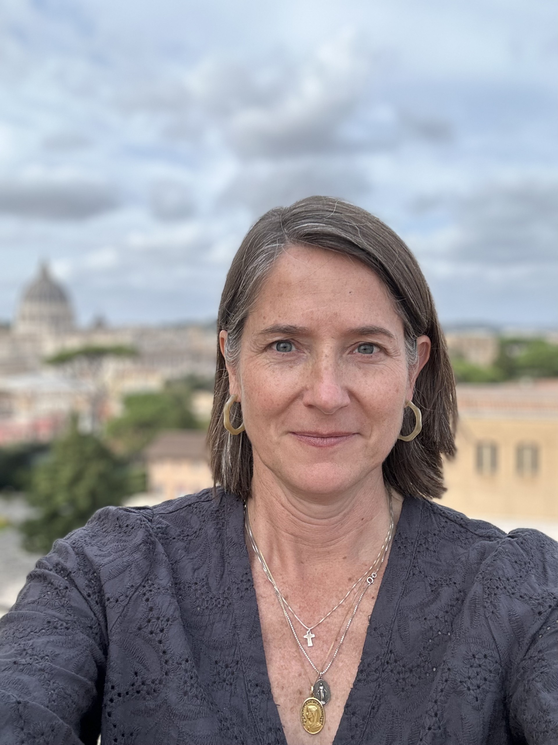 Woman outdoors in Rome with St. Peter’s Basilica visible behind her under a cloudy sky