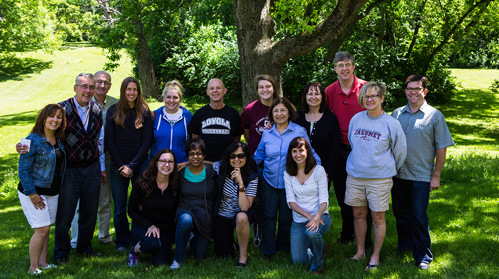 Various faculty and staff members gather for a group photo in front of a tree