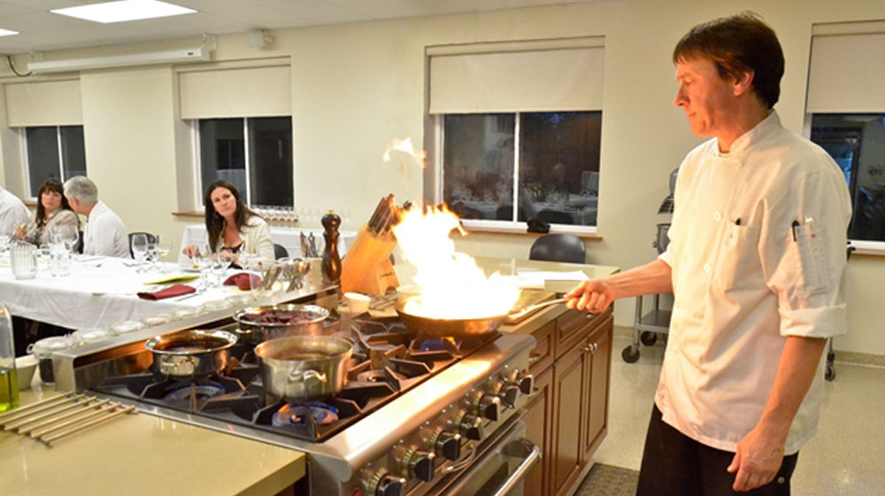 A chef leads a cooking class while handling a sauté pan on fire