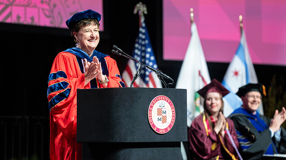 Lorna Finnegan, wearing cap and gown, smiles and claps at the podium