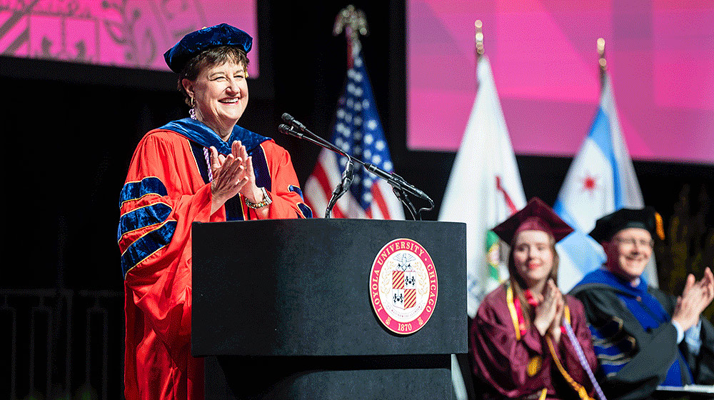  Loyola University Chicago, Marcella Niehoff School of Nursing Dean, Lorna Finnegan, wearing cap and gown, smiling and claping at the podium during 2025 Commencement