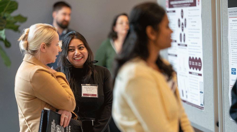 People smile and talk while looking at research posters