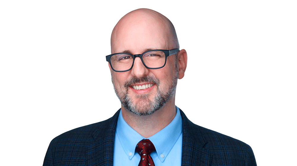 Todd Ruppar, wearing blue dress shirt with coat and tie, smiles.