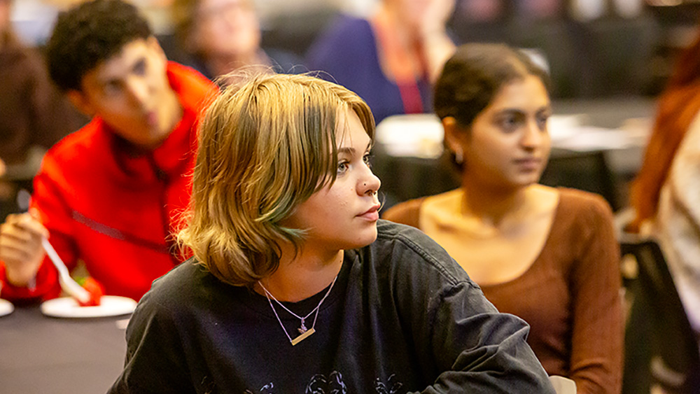 Three students in a classroom setting are listening intently