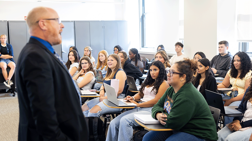Clinical Assistant Professor Matthew Bruder stands in front of a full classroom of students, sitting, and speaks on the first day of the fall 2025 semester.