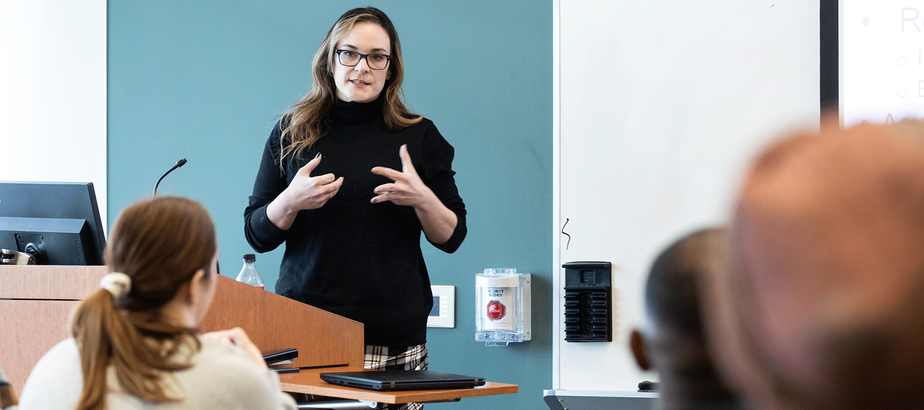 A female faculty member stands in front of a classroom and speaks