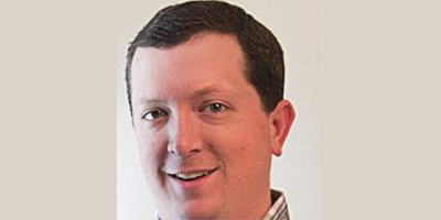 Professional headshot of a smiling man against a light background