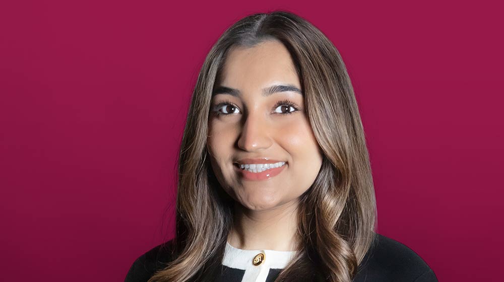 Falak Choudry smiling in front of a maroon background