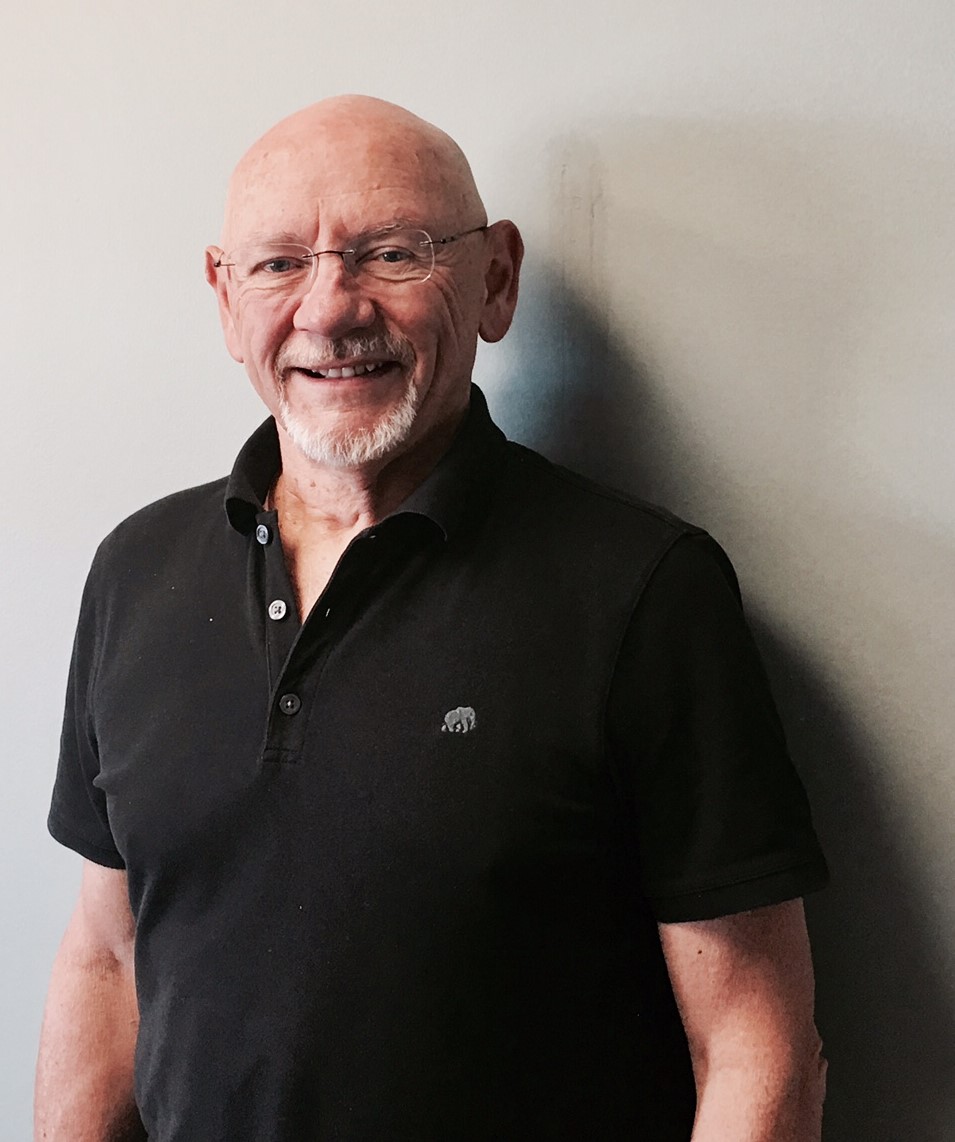 Portrait of a smiling bald man with glasses wearing a black shirt against a plain background
