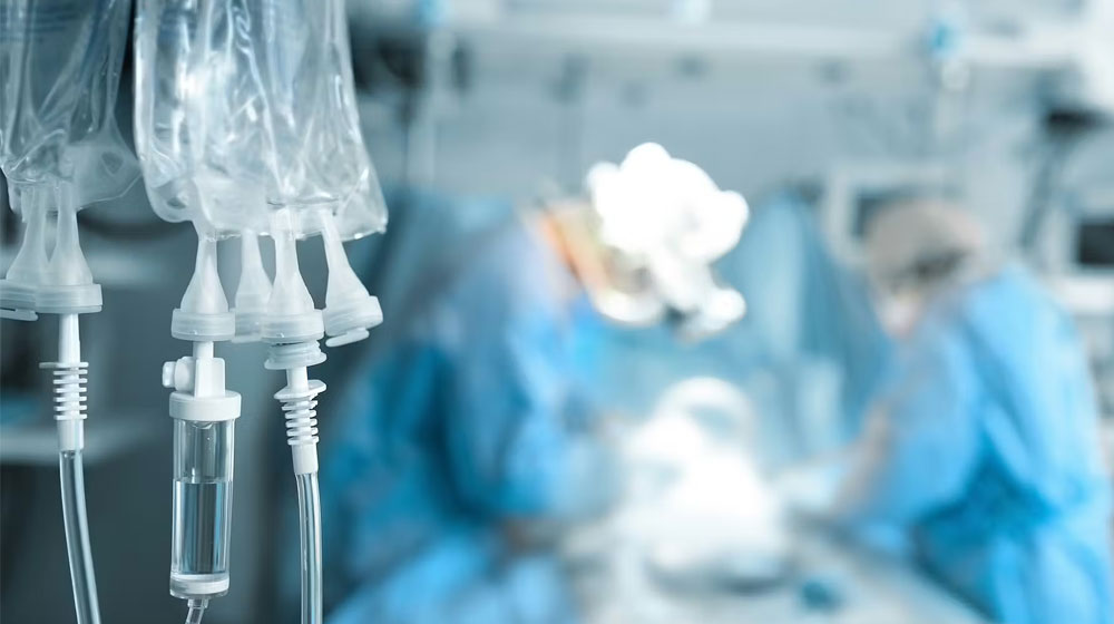 IV bags hanging in an ICU with doctors operating in background