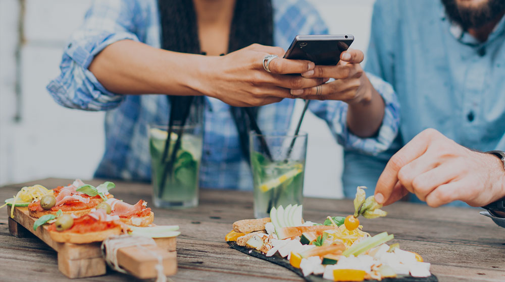 A couple eating a meal, one of them taking a photo of their plate