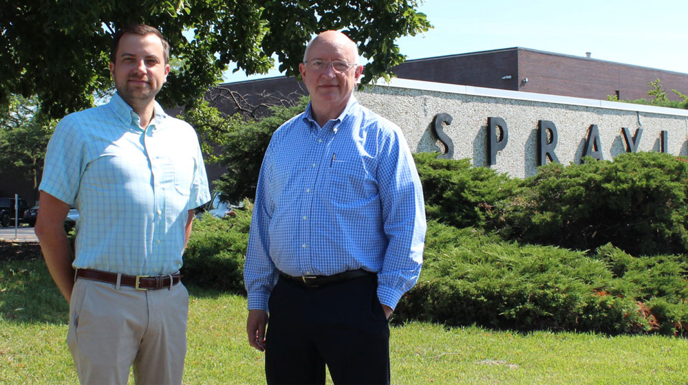 Two men in business attire pose for a photo in front of a commercial landscape.