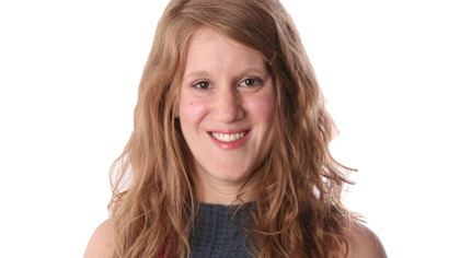 Headshot of a Quinlan faculty member with long blonde hair, smiling, wearing a dark top against a light neutral background.