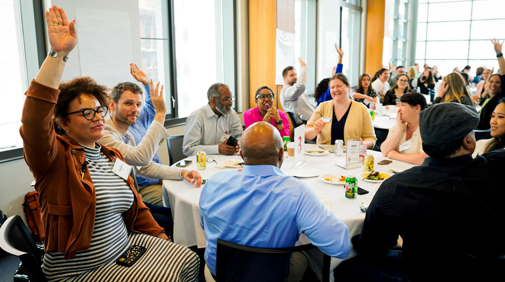 People raising their hands while sitting at round tables