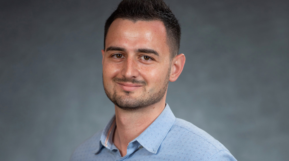 Gabriel Virdaru smiling in front of a blue background