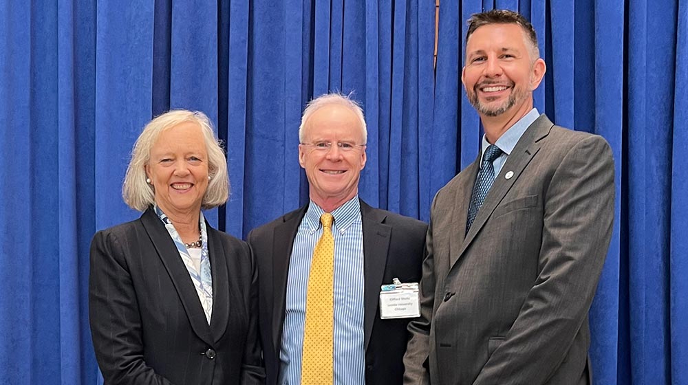 U.S. Ambassador Meg Whitman, Quinlan Professor Cliff Shultz, and Keith Dokho (MBA ’03) standing in front of blue drapes and white chairs
